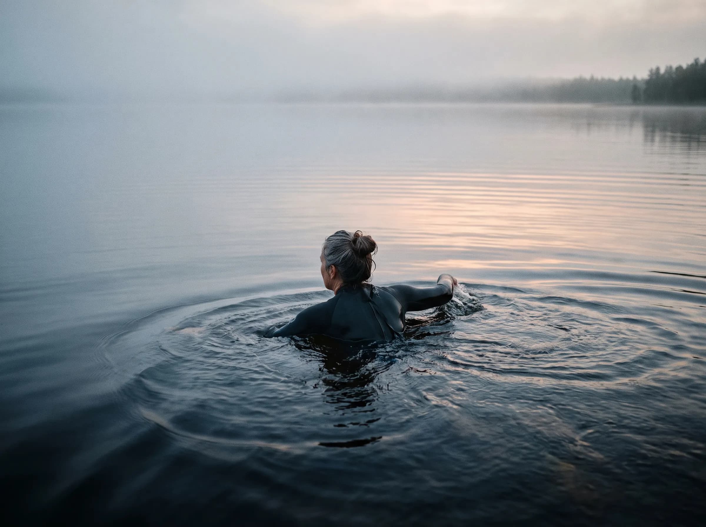 A woman swimming in a calm lake at dawn