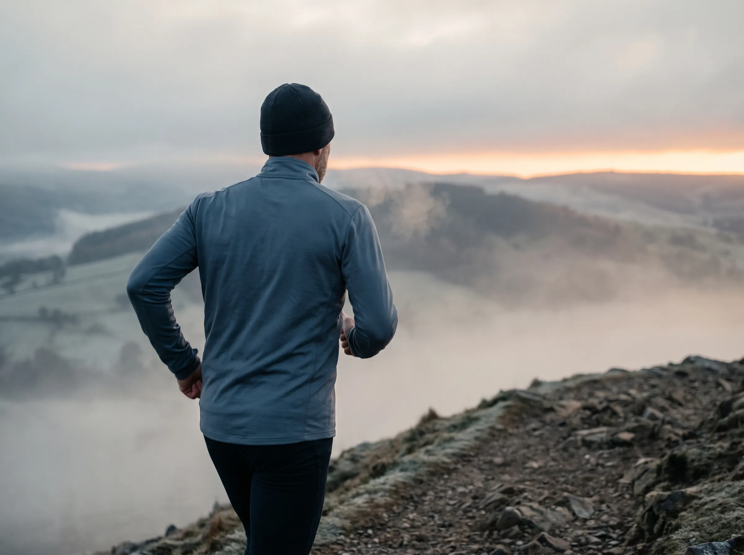 A man trail-running along a misty ridge at dawn